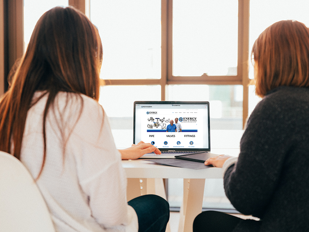 Two women sit at computer looking at the Energy Pipe Website. This photo promotes our blanket orders service.